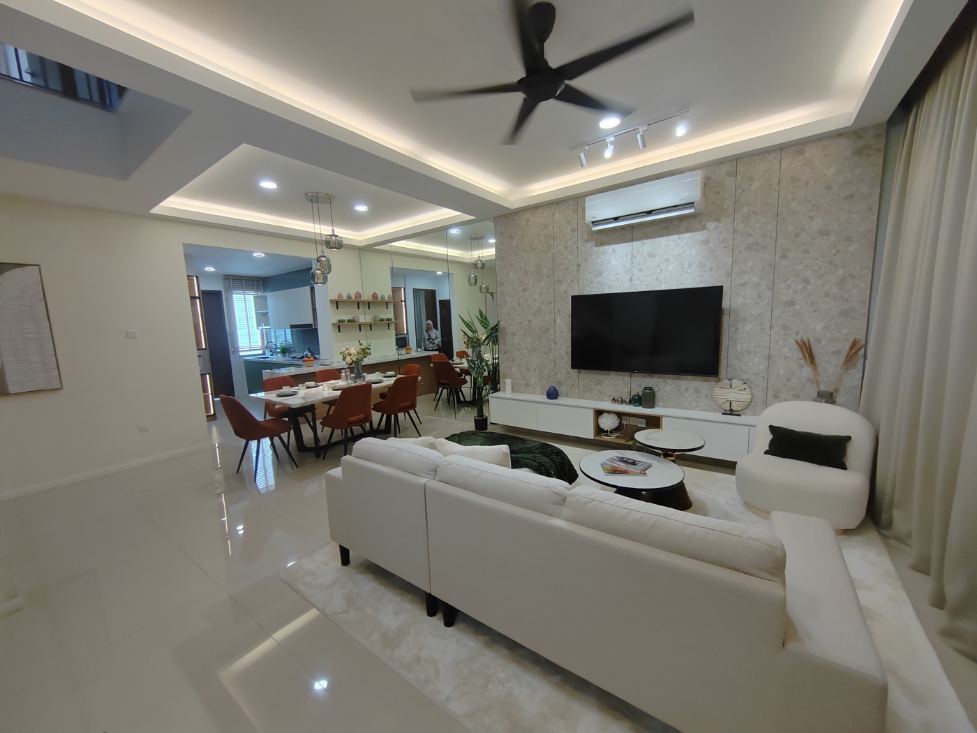Foto ruang tamu rumah contoh Adenia dengan sofa putih, dinding TV dan pandangan ke ruang makan