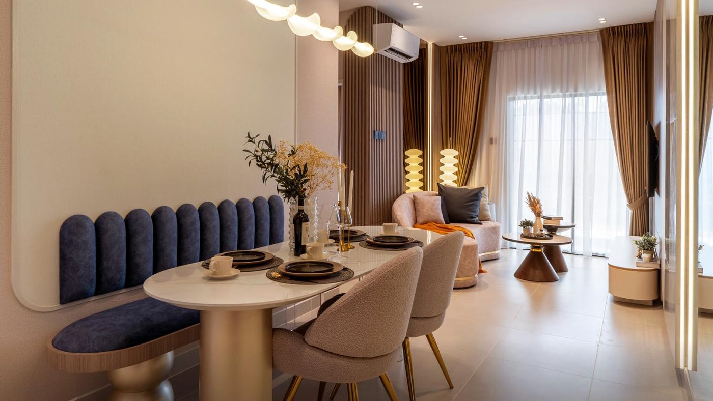 Foto show unit Ara Residences Jenis A: ruang makan dengan kerusi bangku berkusyen biru, meja bujur dan ruang tamu di belakang