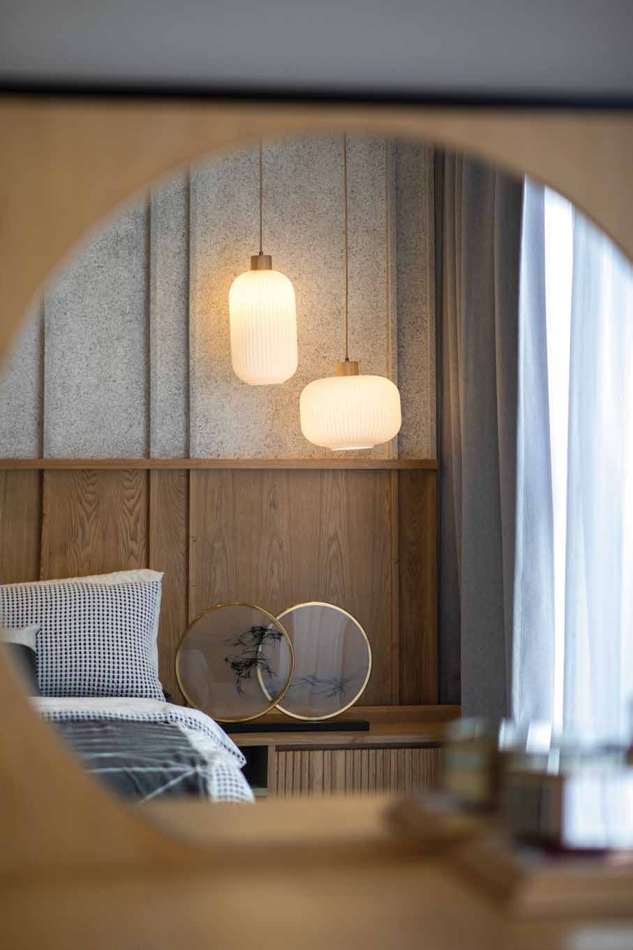 Foto rumah contoh Avela: sudut bilik tidur dengan katil, cermin bulat dan panel kayu