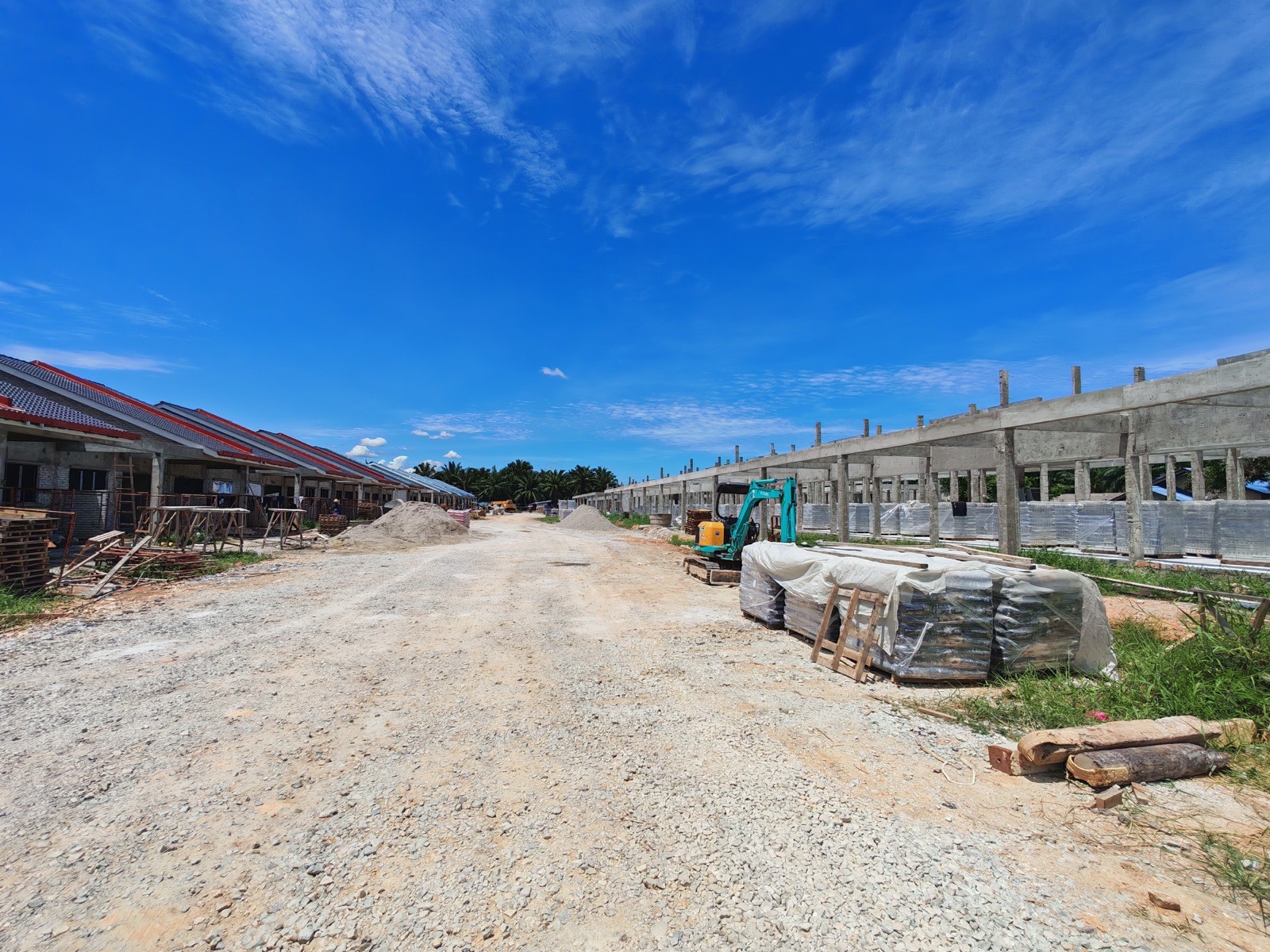 Foto sebenar jalan di tengah tapak dengan rumah berbumbung di kiri dan struktur konkrit di kanan