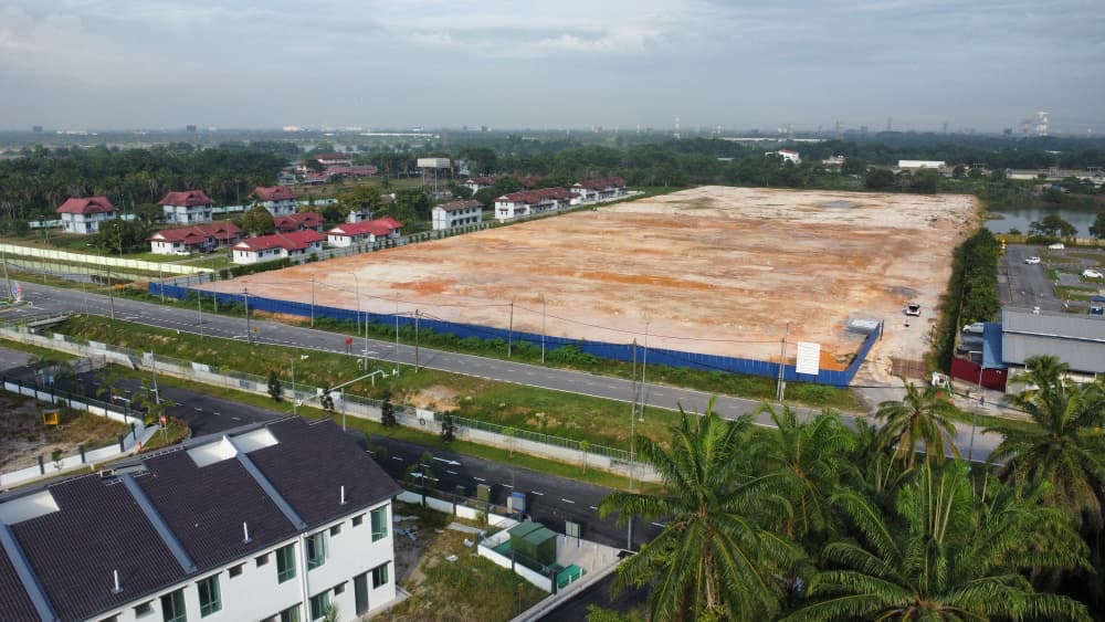 Foto dron sebenar tapak Taman Warisan Hijauan dari sudut lain, menunjukkan tanah rata berpagar di sebelah jalan dan kawasan perumahan sedia ada